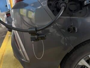 A close-up of an electric vehicle plugged in and charging at a charging station, with the charging cable connected to the car’s port.