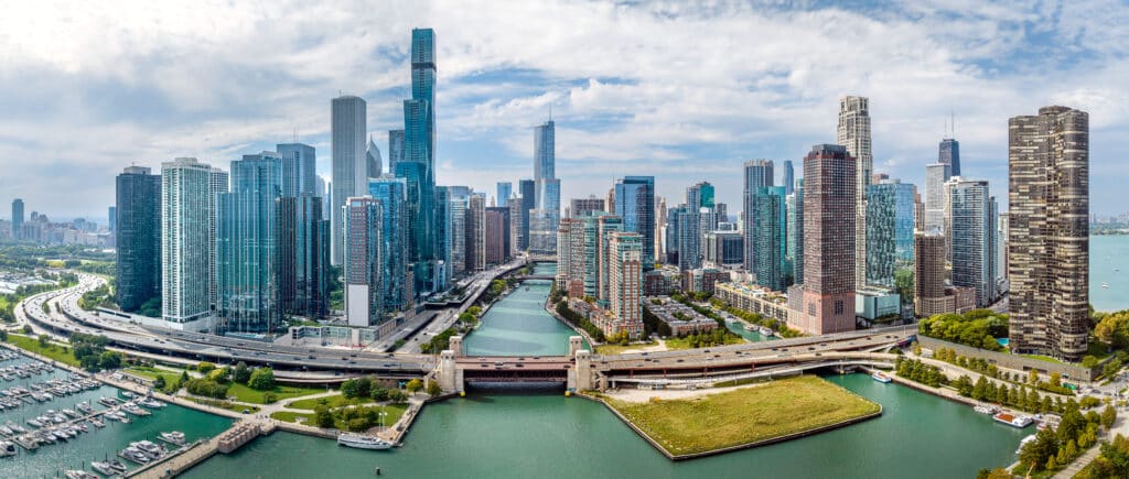 Aerial view of a modern city skyline with high-rise buildings, a river flowing through the center, and a marina on the left.