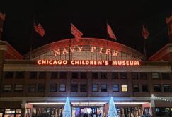 Nighttime view of Navy Pier entrance in Chicago, featuring illuminated signs for Chicago Children's Museum and holiday lights at the entrance.