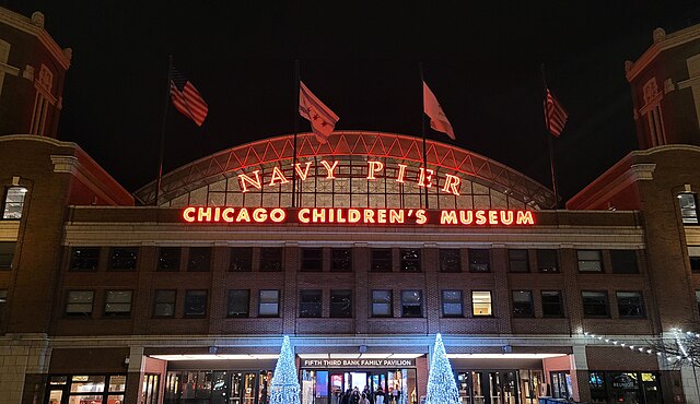 Nighttime view of Navy Pier entrance in Chicago, featuring illuminated signs for Chicago Children's Museum and holiday lights at the entrance.