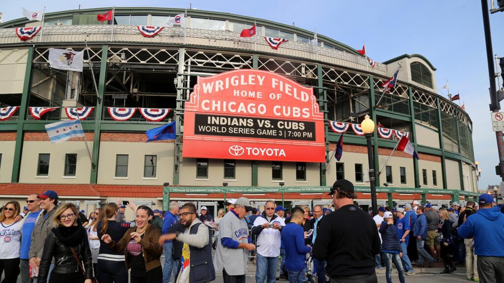 Crowd gathers outside Wrigley Field in Chicago, with a marquee displaying "Indians vs. Cubs World Series Game 3 7:00 PM.