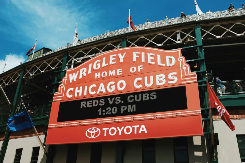 Wrigley Field marquee sign displays "HOME OF CHICAGO CUBS" and advertises a game between the Reds and Cubs at 1:20 PM, sponsored by Toyota.