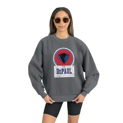 Woman wearing round sunglasses and a gray sweatshirt with the DePaul University logo and mascot, standing with hands on hips against a plain background.