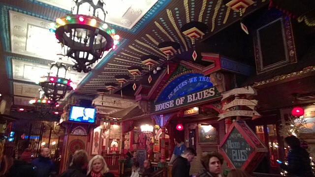 House_of_Blues_Chicago Interior of a lively House of Blues venue with colorful decor, chandeliers, people walking, and a TV screen in the background.