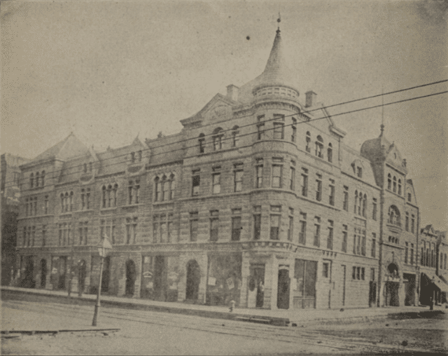 Thalia_Hall,_Chicago Historic photograph of a large, three-story stone building with arched windows and a corner turret on a city street.