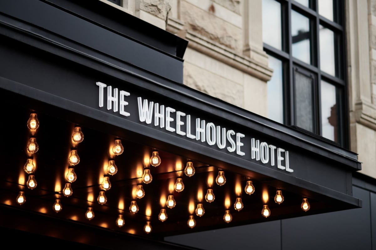 The entrance canopy of The Wheelhouse Hotel with exposed light bulbs hanging from the ceiling and a sign displaying the hotel name.