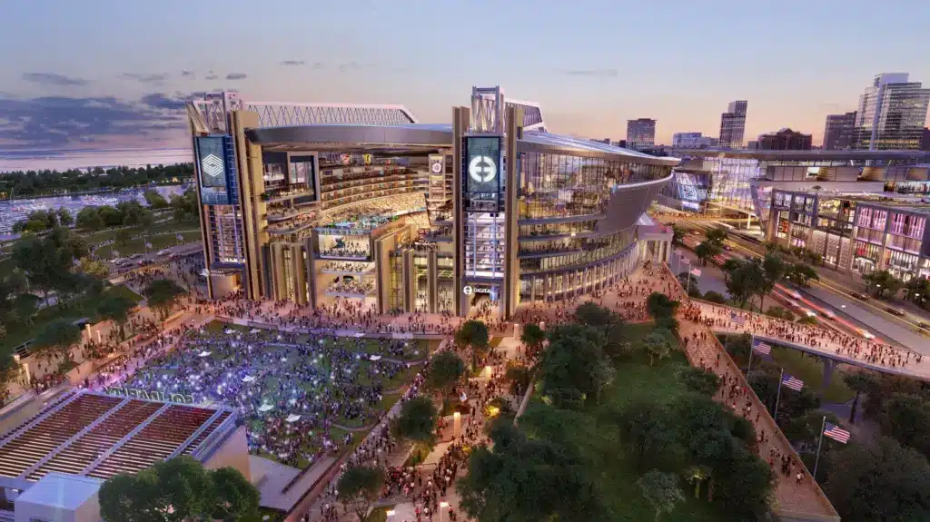A large, modern stadium surrounded by crowds, with adjacent green spaces and city buildings in the background at dusk.