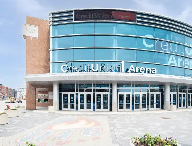 The exterior of Credit Union 1 Arena with blue-tinted glass windows, entrance doors, and the arena name displayed above the entrance.