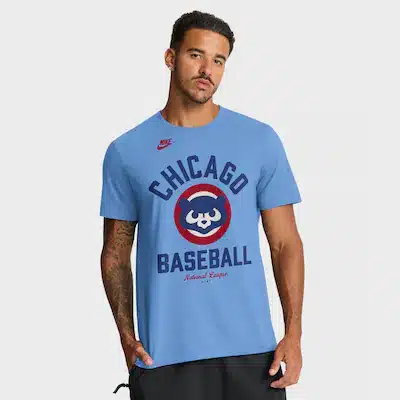 cubs-mens-tshirts Man wearing a light blue t-shirt with a Chicago Baseball logo, a bear symbol, and the words "National League." The t-shirt also has a red Nike logo on the shoulder.
