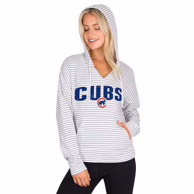 cubs-womens-sweatshirts Woman wearing a white and gray striped hoodie with "CUBS" and the Chicago Cubs logo on the front, standing with one hand in her pocket.