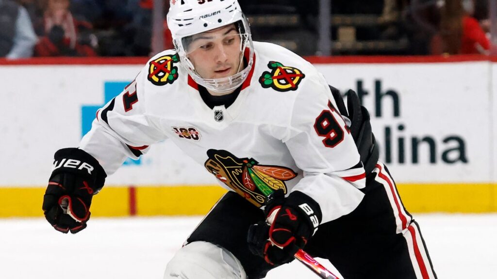 A hockey player in a white Chicago Blackhawks uniform skates on the ice during a game, focused on the action.