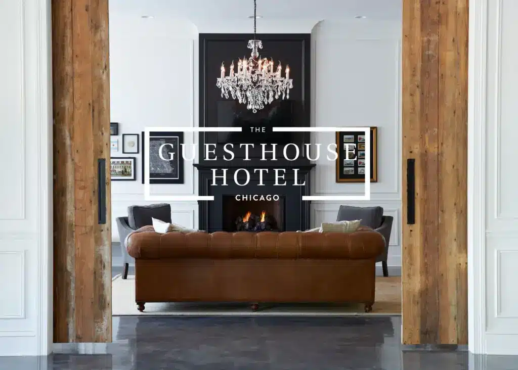 A brown leather sofa faces a fireplace and chandelier in a chic living area at The Guesthouse Hotel, Chicago.