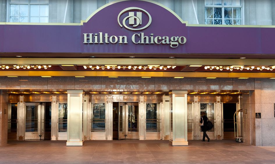 Front entrance of Hilton Chicago hotel with gold-framed revolving doors, a purple and gold sign, and a person entering.