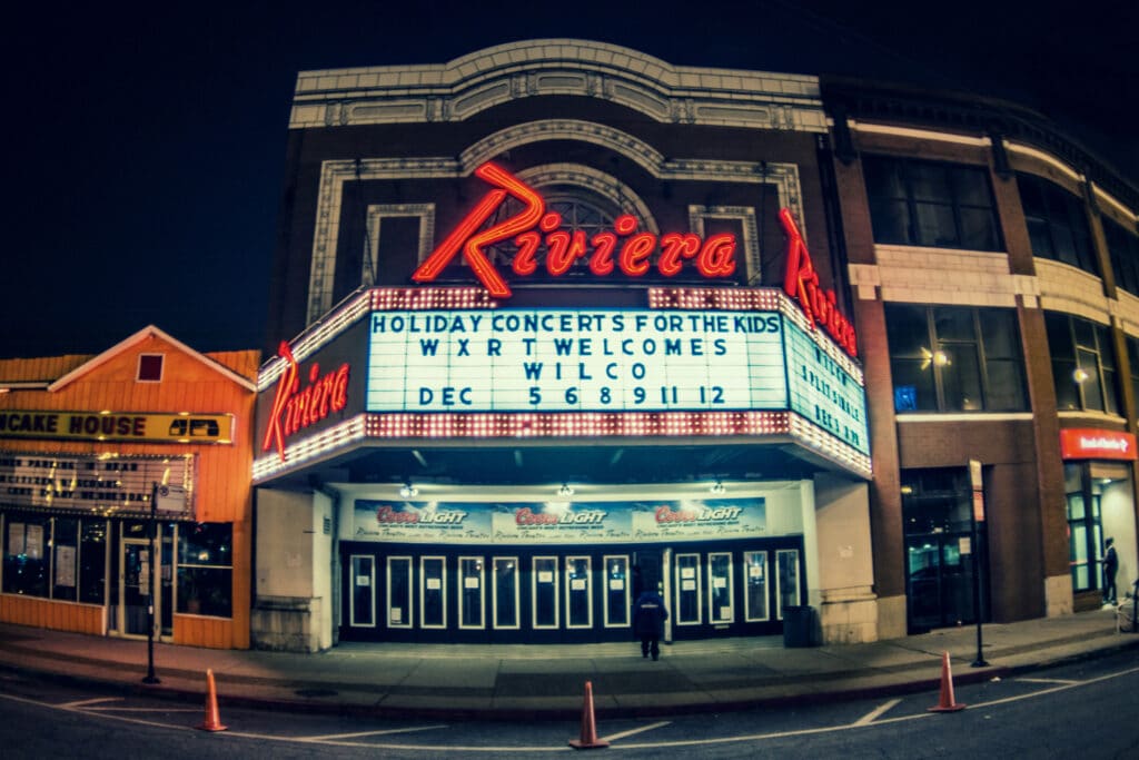 The marquee of the Riviera Theatre at night displays "Holiday Concerts for the Kids, WXRT Welcomes Wilco, Dec 5 6 8 9 11 12.